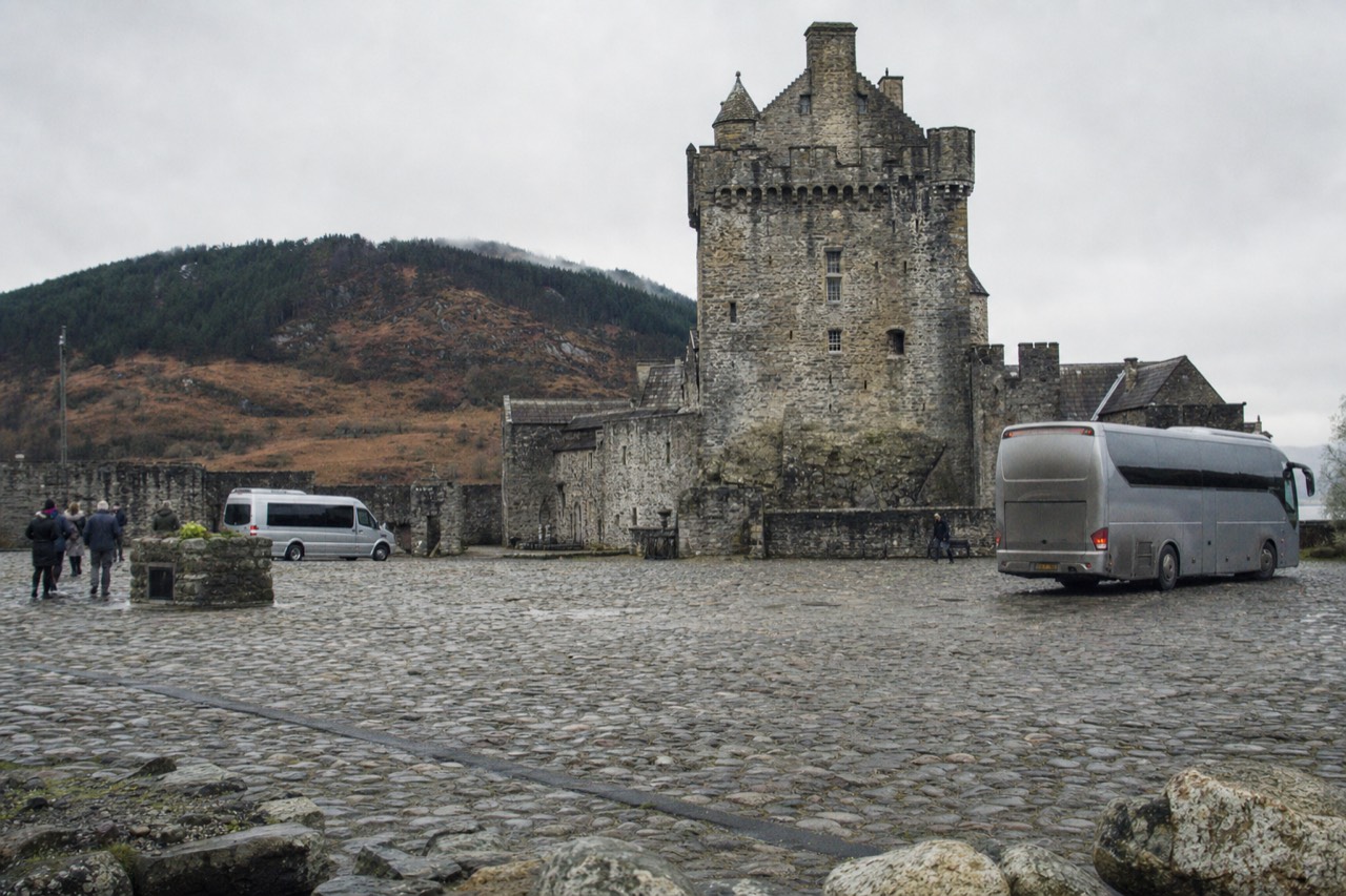 A stone tower house with a cobbled courtyard under grey cloud, the kind of Lowland castle used as a television filming location.
